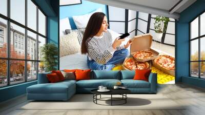 Young woman with mobile phone taking picture of tasty pizza in bedroom Wall mural