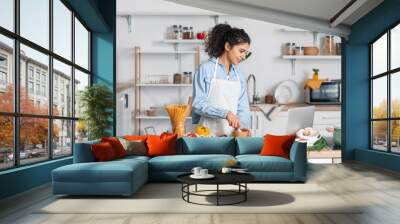 Young woman with mortar and pestle using laptop in kitchen Wall mural