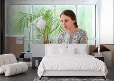 Young woman with parcels using laptop in office Wall mural