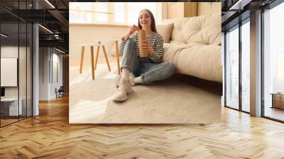 Young woman with potato chips sitting on floor at home Wall mural