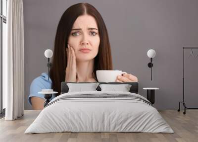 Young woman with sensitive teeth and cup of hot coffee on grey background Wall mural