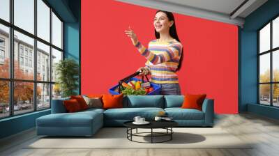 Young woman with shopping basket on color background Wall mural