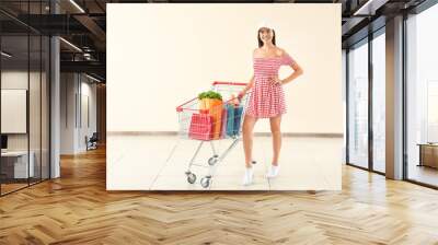 Young woman with shopping cart near light wall Wall mural