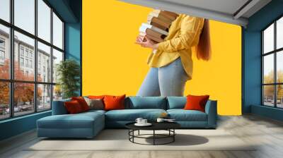 Young woman with stack of books on yellow background Wall mural