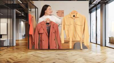 Young woman with stylish outwear near clothes rack at home Wall mural