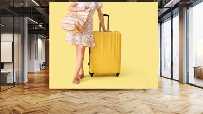 Young woman with suitcase and bag on yellow background Wall mural