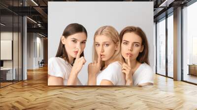 Young women with beautiful makeup showing silence gesture on light background Wall mural