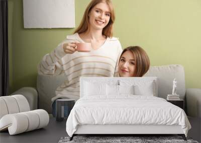 Young women with cups of tea sitting on sofa at home Wall mural