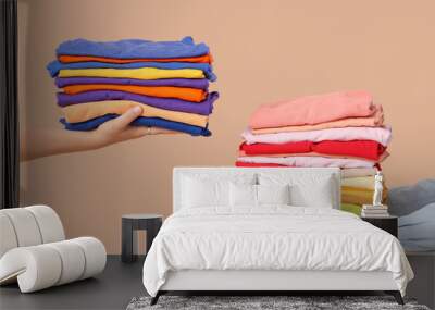 Young women with stacks of colorful clothes on beige background Wall mural