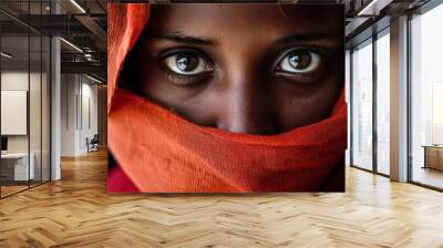 Intense Gaze Under Red Veil. Close-up photo of a young woman with deep brown skin, her eyes visible beneath a vibrant red veil, conveying mystery and depth.
 Wall mural