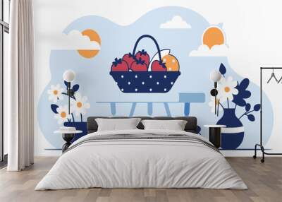 A basket filled with fruit sits on a table outdoors beside a vase of flowers Wall mural