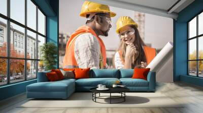 civil engineers working at construction site wearing safety glasses, jacket and helmet checking progress on blueprint Wall mural