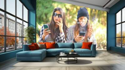 two girls smoking cigarettes and using smart phones. concept of addiction to smoking and smart phone dependency.. Wall mural