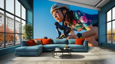 close up asian woman with athletic body shape in protective helmet and glasses riding bicycle on blue sky Wall mural