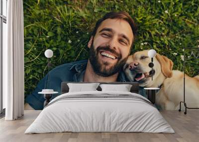 Happy man is laying on the grass with his dog, top view Wall mural