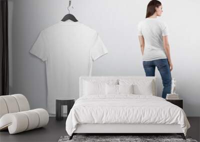 Hanging plain white t shirt on wall. Beside standing rear view of female model in blue denim jeans pant.  Wall mural