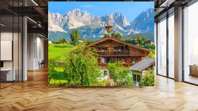 Typical wooden alpine house against Alps mountains background on green meadow in Going am Wilden Kaiser village on sunny summer day, Tyrol, Austria Wall mural