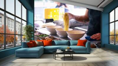 Bowls of ramen on a countertop in a kitchen with steam smoke of boiling noodles, hands put noodles into a bowl with all ingredients to preparing Japanese ramen to serve in a restaurant  Wall mural