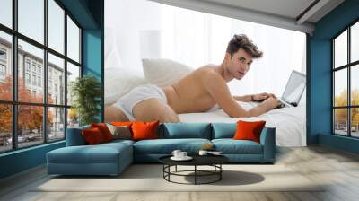 Hot shirtless man using a laptop computer lying in bed wearing underwear. Wall mural