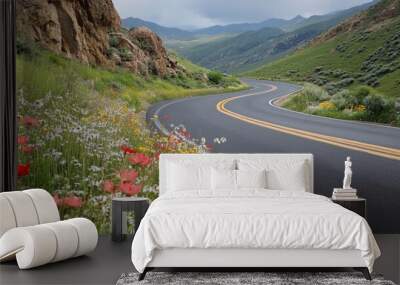 A close-up of a mountain road with smooth, curving asphalt, flanked by blooming wildflowers and rocky outcrops, highlighting the scenic details of the route. Wall mural