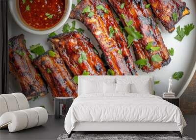 A top-down view of grilled pork ribs on a white plate, garnished with fresh herbs and paired with a small bowl of dipping sauce, ready to serve. Wall mural