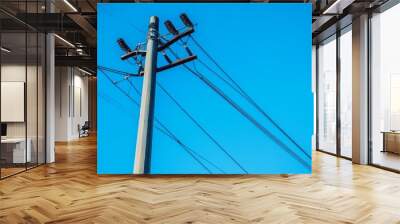 Close-up of a high-voltage power pole with insulators and cables, clear blue sky background Wall mural