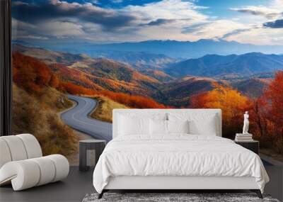 Close-up of a picturesque mountain road with sharp curves and stunning vistas of distant mountain ranges, framed by vibrant autumn foliage. Wall mural