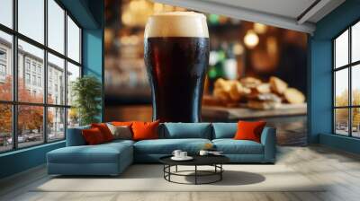 Detailed view of a pint of dark stout beer with a creamy head, served in a pub setting with a wooden table and a few snacks in the background. Wall mural