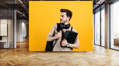 Caucasian young man wearing t-shirt posing isolated over yellow background looking to the side with backpack. Wall mural