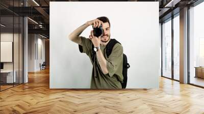 Cheerful caucasian man wearing casual clothes posing isolated over white background taking images with dslr camera. Photographer covering his face with the camera. Wall mural