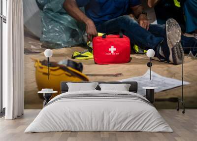 Emergency staff in safety suit use first aid kit to help a man who has an accident in factory workplace, First aid training in industrial company. Wall mural