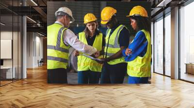 Group of diverse warehouse worker in safety suit, Project manager using blueprint and digital tablet to discussing with engineer team for work in construction industry. Teamwork and unity concept. Wall mural