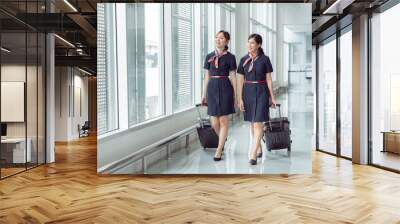 Two beautiful asian woman working in flight attendants in uniform dragging her luggage to airport terminal, people working together with teamwork in customer service. Wall mural