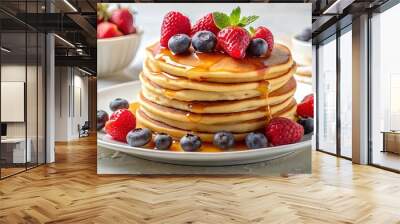 Fluffy pancakes topped with maple syrup and fresh berries on a white plate in natural daylight Wall mural