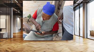 village african old woman learning to use a mobile phone with the help of a volunteer Wall mural