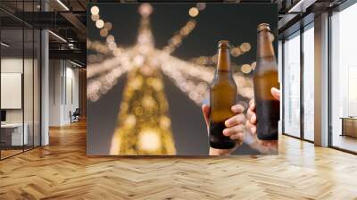 Hands holding beer bottles and happy enjoying harvest time together to clinking glasses at outdoor party on beautiful bokeh night light background.Celebration drinking beer in pub orbar.          Wall mural