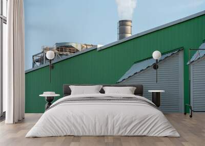 An industrial building and a chimney with white smoke against a blue sky. Air pollution from the smoke of a working factory. Chemical industry and the risk of environmental disaster. Wall mural