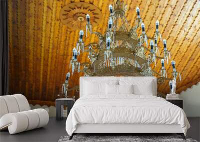 An old antique chandelier hangs on the ceiling of an ancient temple. An elegant chandelier on the background of a wooden ceiling. The interior of the Catholic church. Wall mural