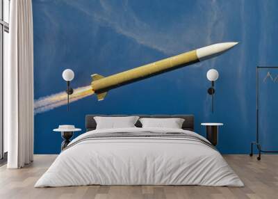 A military rocket is flying through the blue sky. The rocket is leaving a trail of smoke behind it Wall mural