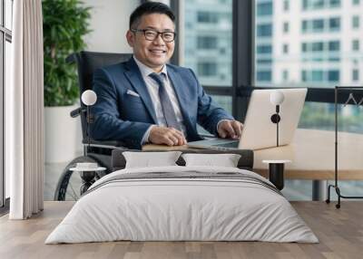 Disabled Asian businessman in a suit and wheelchair, smiling and working with a laptop in a modern office Wall mural