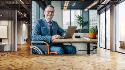 Disabled European businessman in a suit and wheelchair, smiling and working with a laptop in a modern office Wall mural