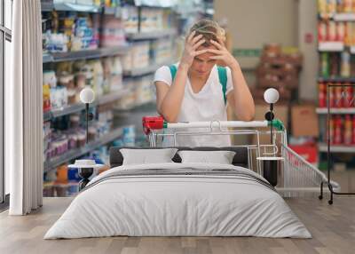 Upset woman in a supermarket with an empty shopping trolley. Crises, rising prices for goods and products. Woman shopping at the supermarket. Wall mural