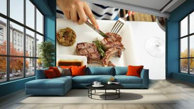 grilled meat loin in a square plate with sauce is cut with utensils in female hands
 Wall mural