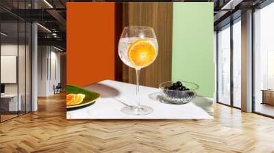 Gin tonic cocktail, garnished with orange slice, colorful background Wall mural