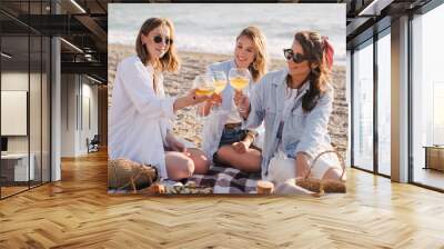 Three young beautiful happy women female friends having cozy summer picnic with lemonade, fresh bread and fruits on a beach. Wall mural