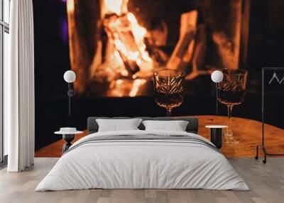 Two glasses of red wine on wooden table with cozy fireplace flame on the background. Wall mural