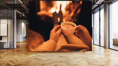 Woman drinkink hot cocoa sitting by the fire in front of cozy fireplace. Wall mural