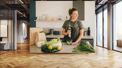 Young woman making smoothie at the kitchen, using blender and fresh fruits and vegetables. Wall mural