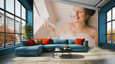 Young woman taking bath with foam near big window. Wall mural