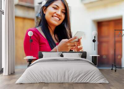 smiling latin woman with flower in her hair sitting by a fountain typing on a phone Wall mural